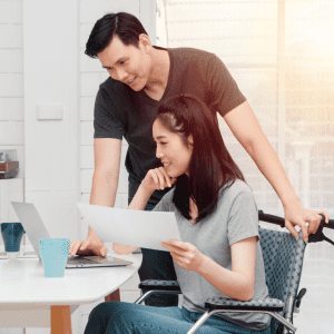 A physically challenged woman on a wheelchair and looking at the computer along with her spouse to sign up for disability insurance in Ontario, Canada from DFSIN Toronto West (Orlando Ali Financial)