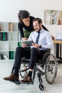 A long-term disabled self-employed man is sitting on a wheelchair along and happily smiling with his spouse because he subscribed to long-term disability insurance with DFSIN Toronto West and he saved his hard-earned money